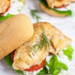 Walleye sandwiches on buns with tartar sauce, lettuce, tomatoes, and fresh dill.