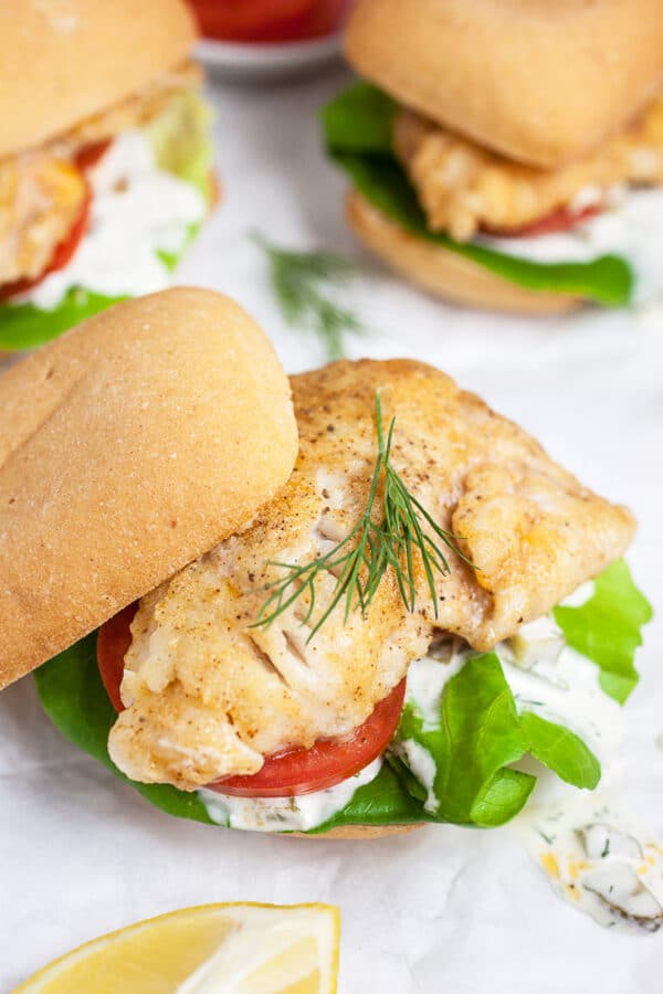 Walleye sandwiches on buns with tartar sauce, lettuce, tomatoes, and fresh dill.