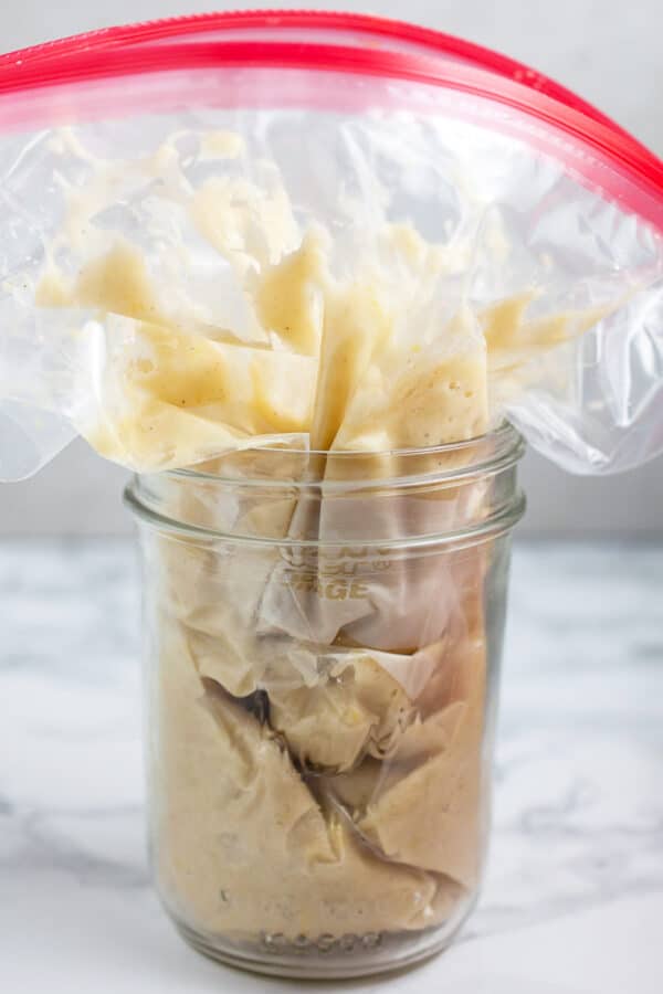 Doughnut batter in plastic freezer piping bag placed in glass mason jar.