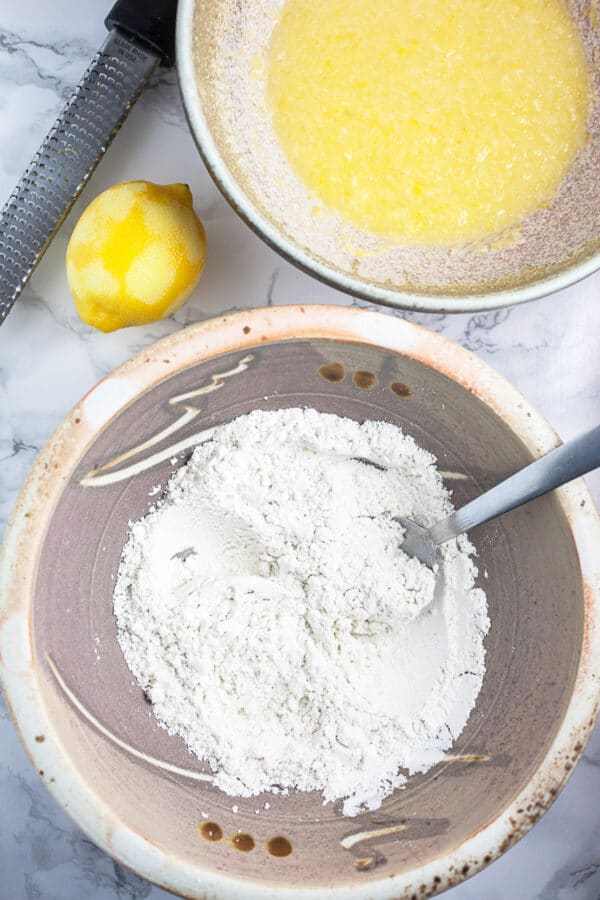 Wet and dry doughnut ingredients in two separate ceramic bowls with zested lemon.