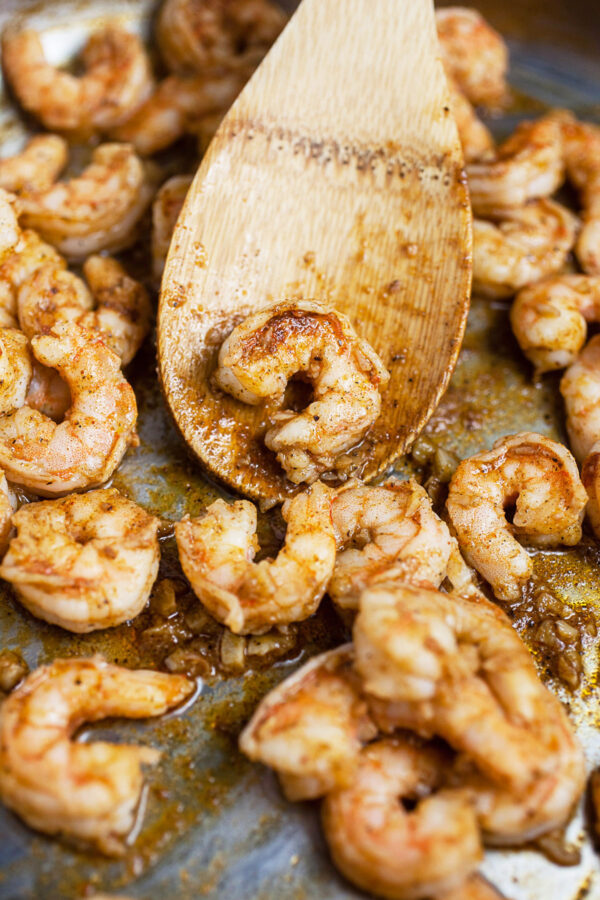 Sautéed shrimp in skillet with wooden spoon.
