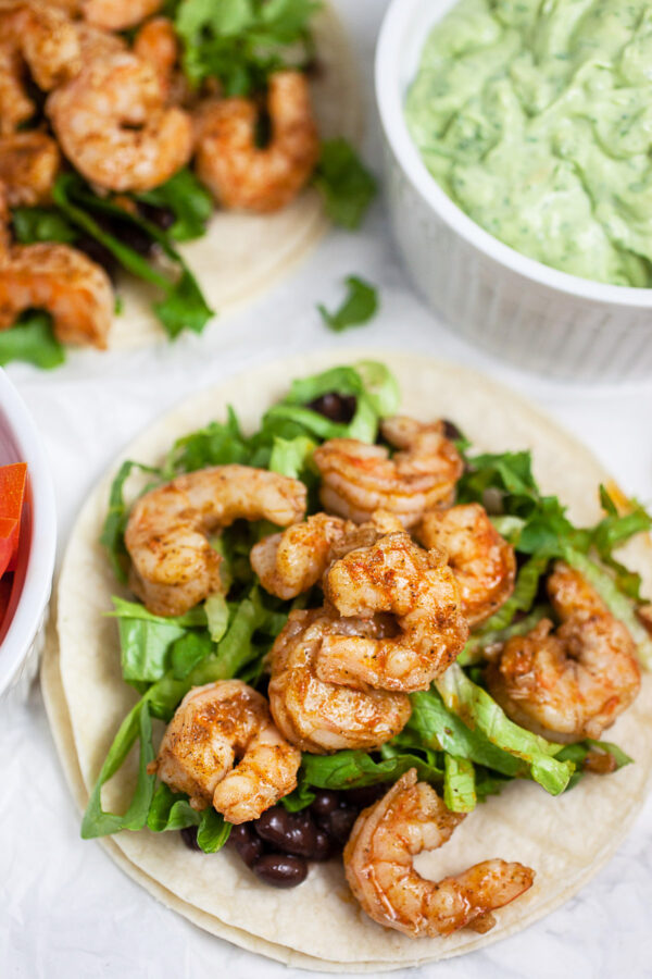 Shrimp tacos with lettuce and black beans on corn tortillas.