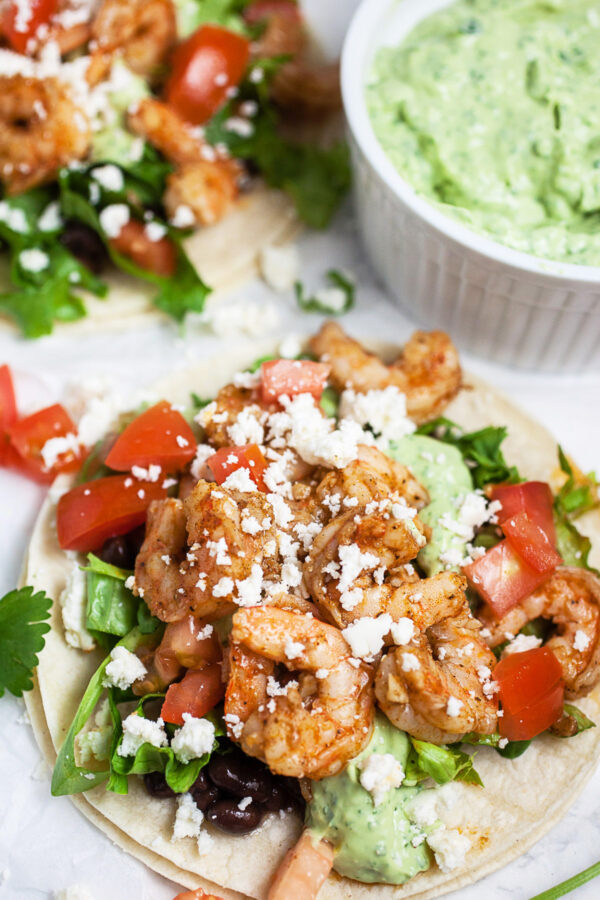 Cajun shrimp tacos on corn tortillas with black beans, lettuce, diced tomatoes, avocado sauce, and queso fresco.