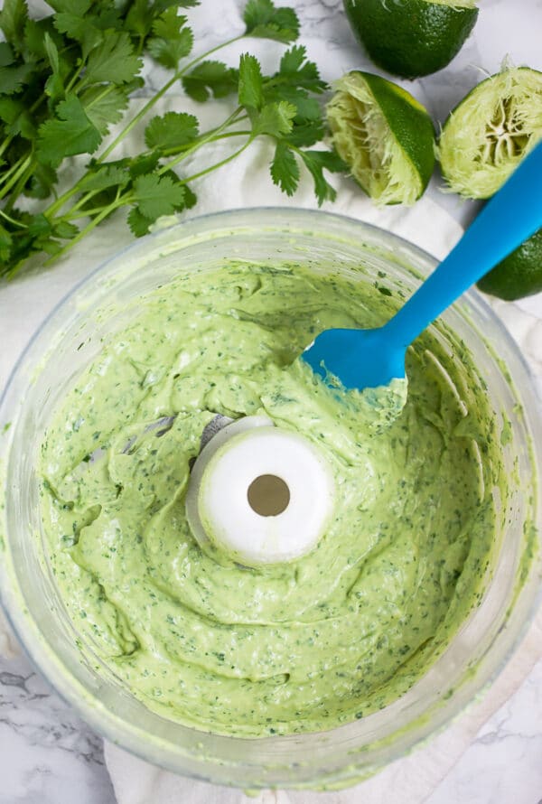 Cilantro lime avocado cream sauce in food processor with blue spatula.