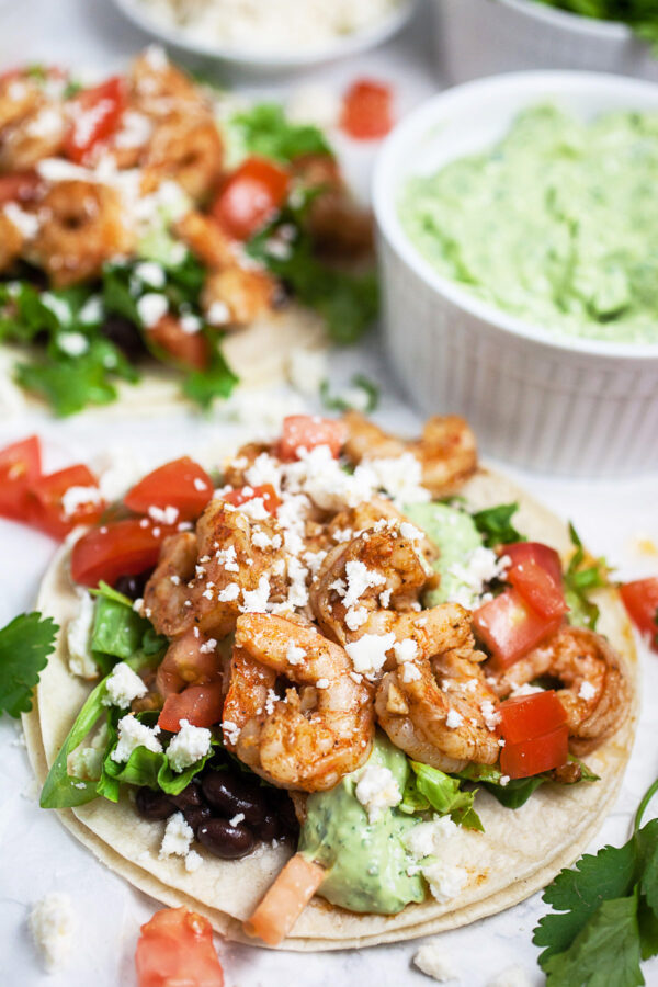 Cajun shrimp tacos with black beans and avocado sauce garnished with tomatoes and cilantro.