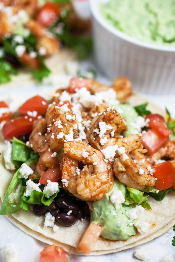 Cajun shrimp tacos with avocado sauce, diced tomatoes, black beans, and queso fresco on corn tortillas.