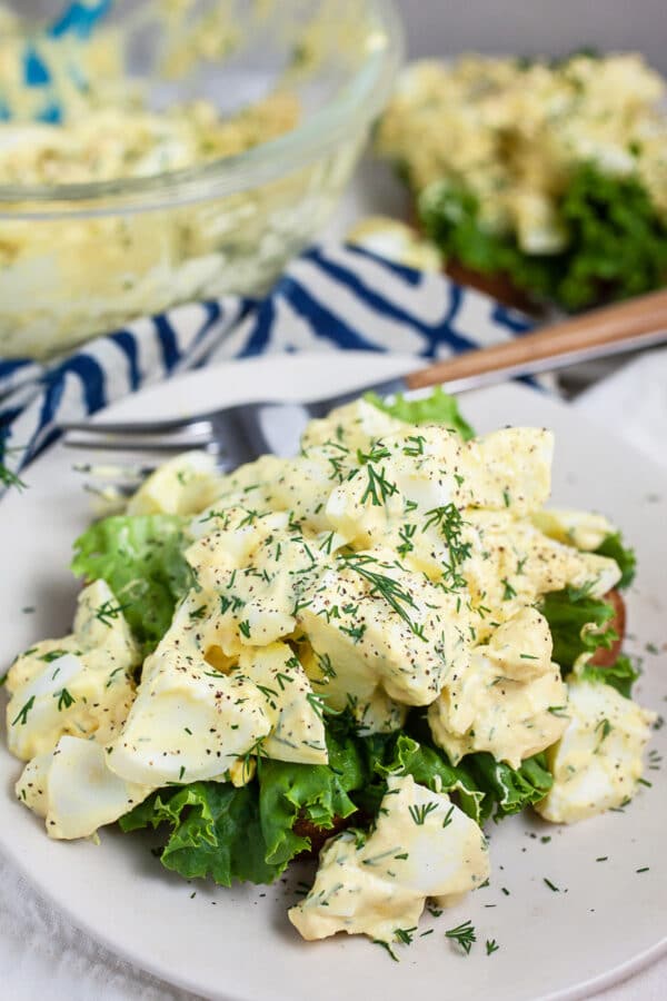 Egg salad on bread and lettuce on white plate with fork.