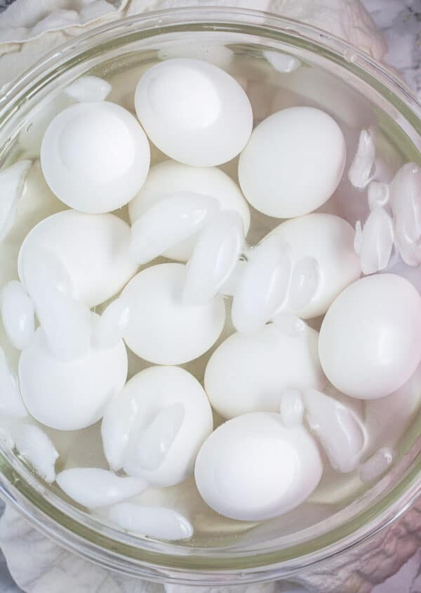 White eggs in ice water bath in glass mixing bowl.