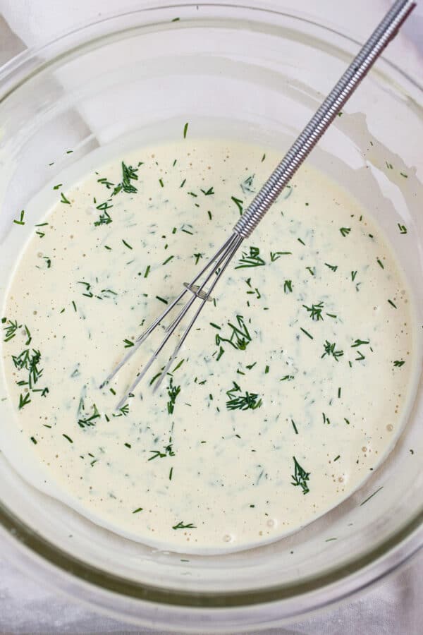 Creamy lemon dill dressing in small glass bowl with whisk.