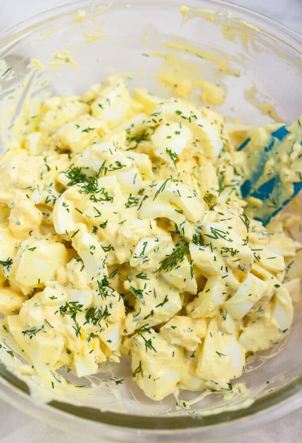 Egg salad with dressing in large glass mixing bowl garnished with fresh dill.