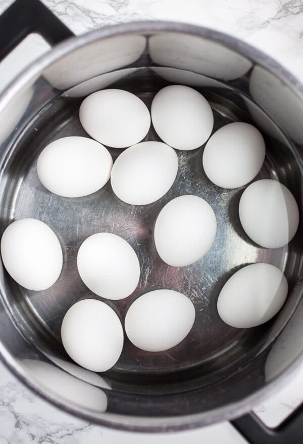 White eggs in boiled water in metal pot.