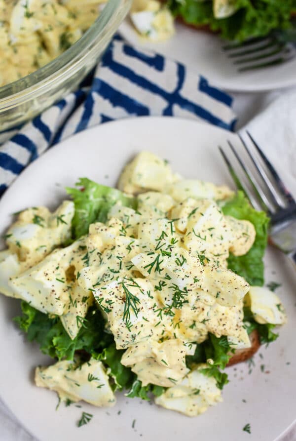 Lemon dill egg salad on bread with lettuce on small white plate with fork.