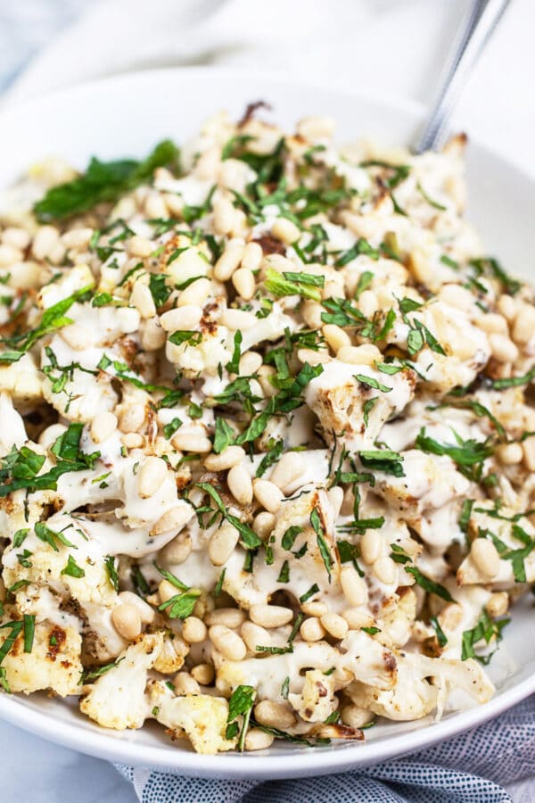 Mediterranean lemon tahini roasted cauliflower in white bowl with spoon garnished with fresh mint.