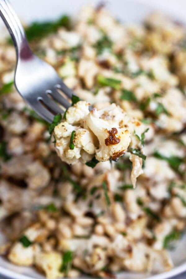 Roasted cauliflower on fork lifted from white bowl.