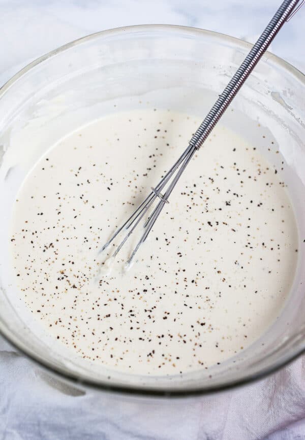 Lemon tahini dressing in small glass bowl with whisk.