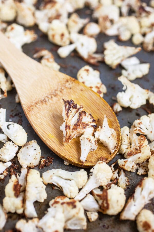 Roasted cauliflower on metal baking sheet with wooden spatula.