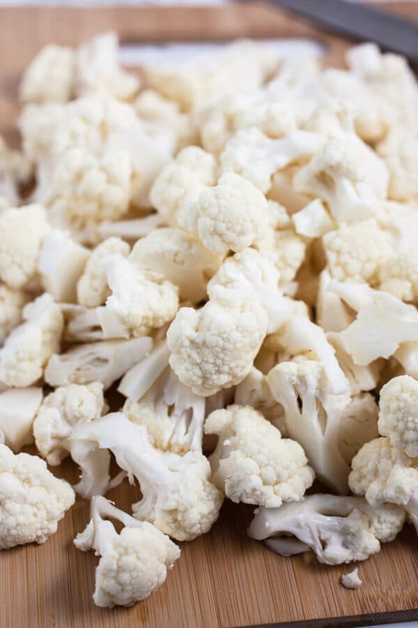 Cauliflower florets on wooden cutting board.