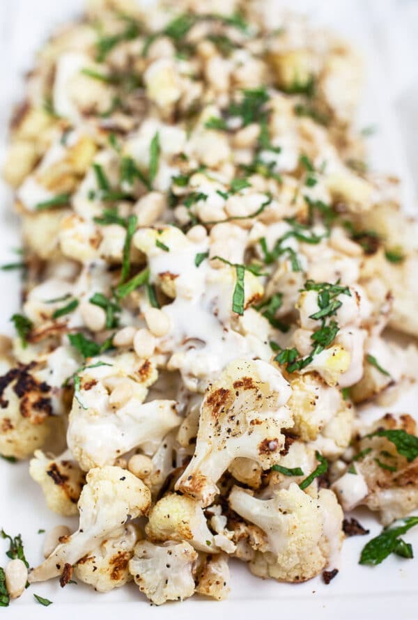 Roasted cauliflower with tahini sauce and fresh mint on white serving platter.