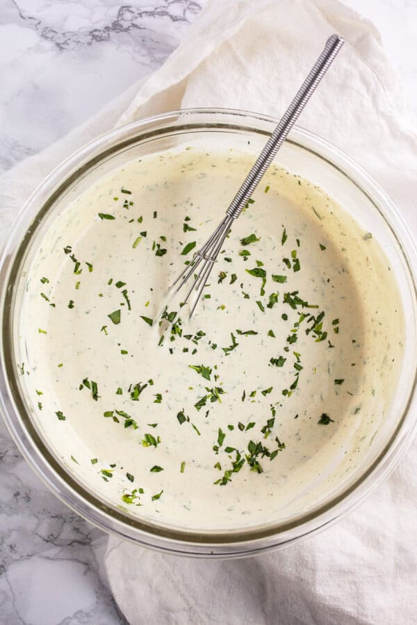 Sour cream tarragon sauce in small glass bowl with whisk.