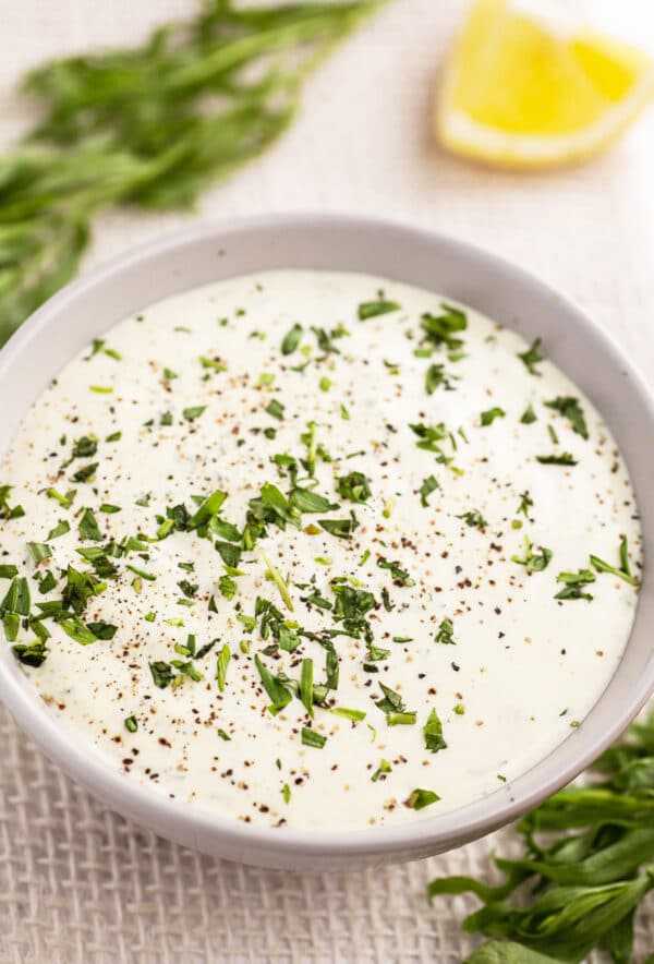 Sour cream tarragon sauce with lemon wedge and fresh tarragon in small bowl.