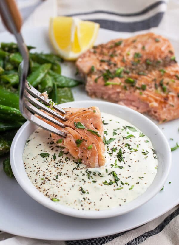 Salmon on fork dipped into small bowl of tarragon sauce.