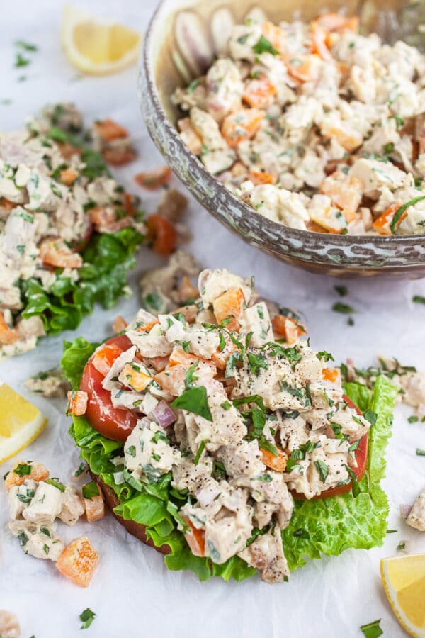 Lemon basil chicken salad with lettuce and tomato on white surface with lemon wedges.