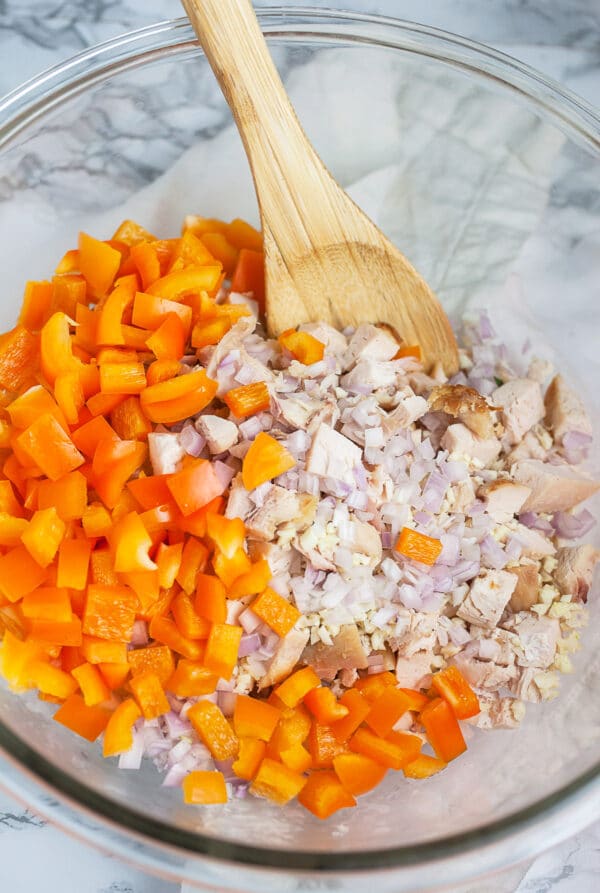 Diced chicken, garlic, shallots, and orange bell peppers in large glass mixing bowl.