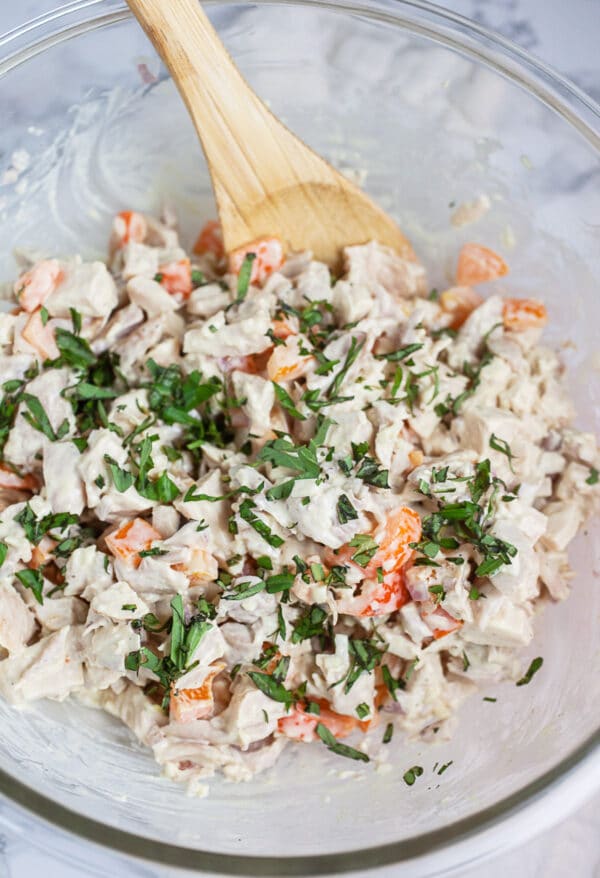 Chicken salad ingredients with fresh minced basil in glass mixing bowl.