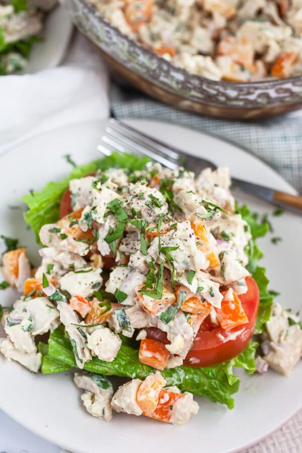 Lemon basil chicken salad with lettuce and tomatoes on small white plate with fork.