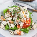 Lemon basil chicken salad with lettuce and tomato on small white plate with fork.