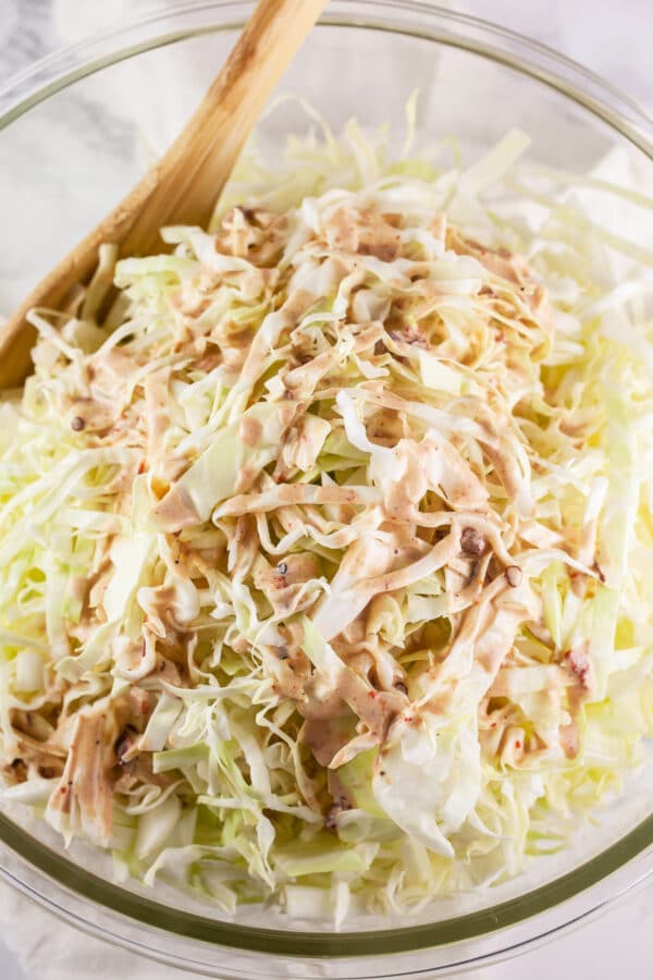 Chipotle dressing on shredded green cabbage in large glass bowl.