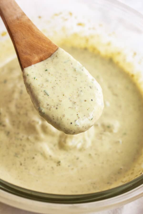 Basil pesto mayo on wooden spoon lifted from small glass bowl.