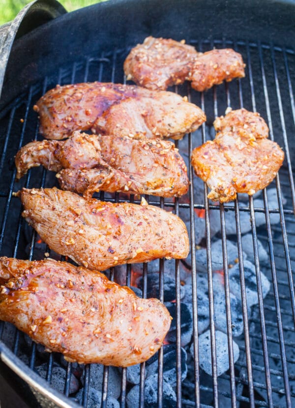 Raw chicken breasts cooking on Weber grill.