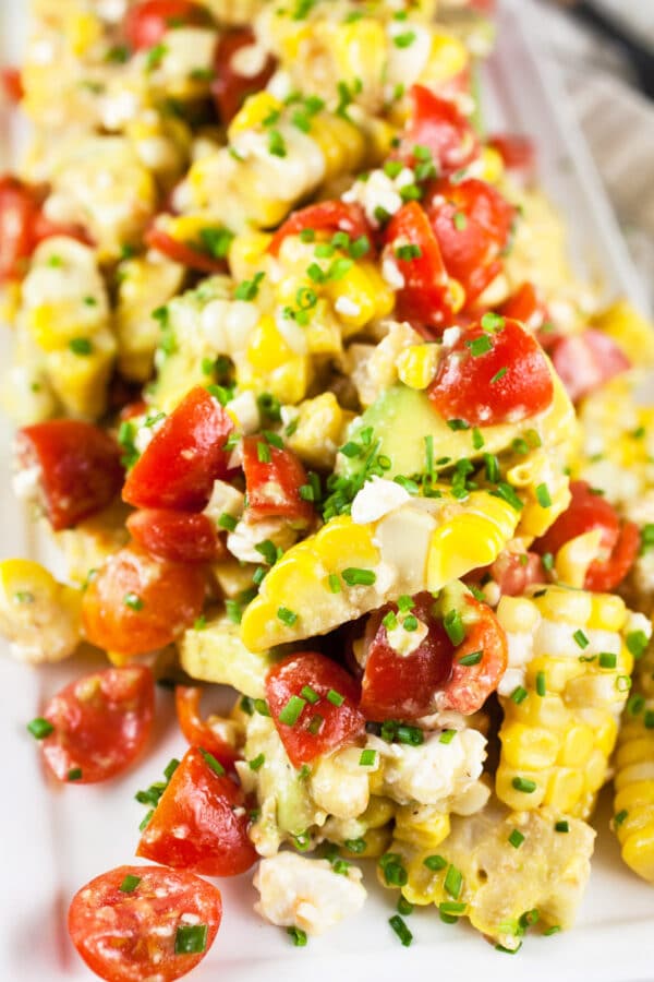 Grilled corn, tomato, and avocado salad in feta dressing on white serving platter.