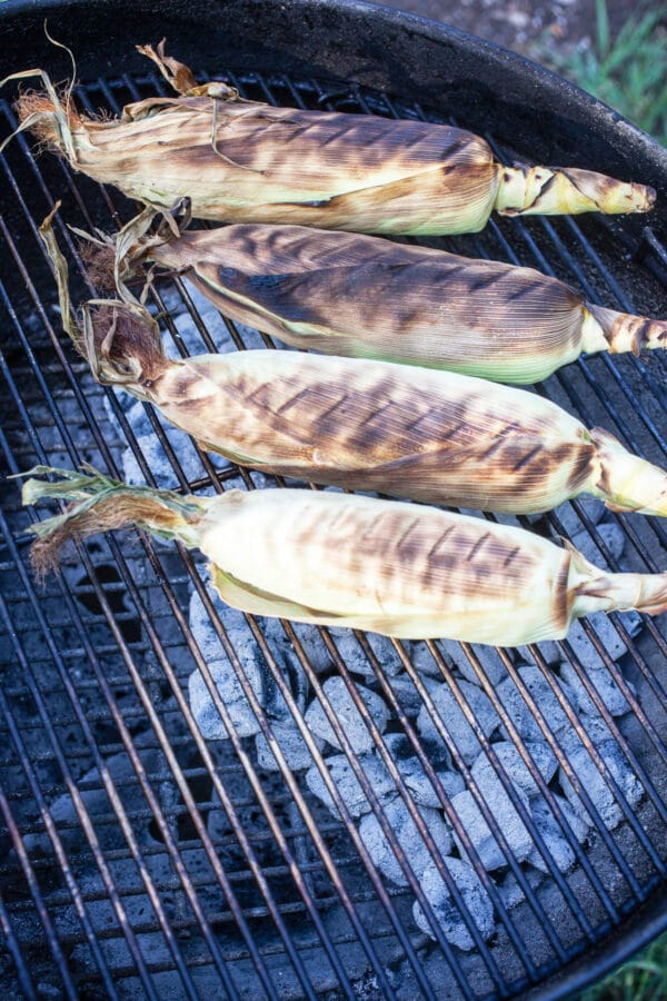 Charred corn cobs in husks on Weber grill.