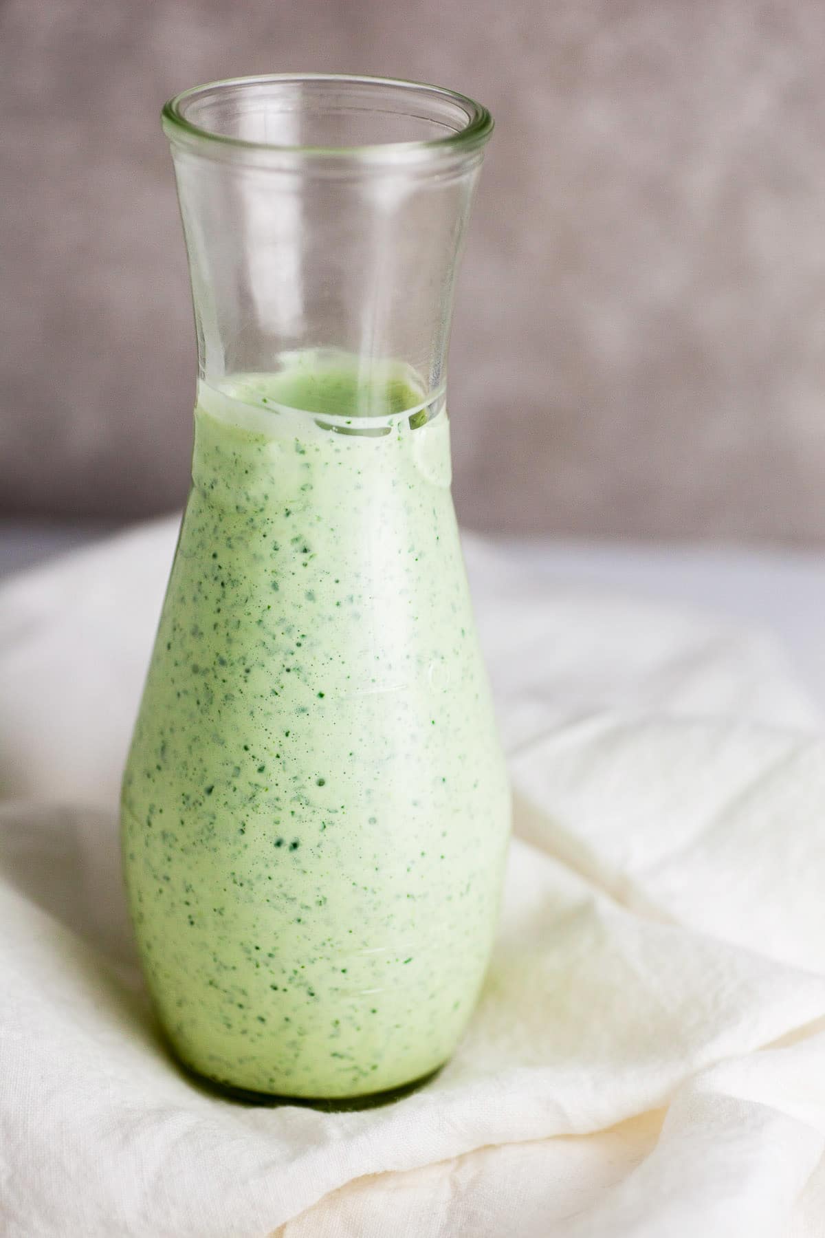 Creamy cilantro lime dressing in glass jar on white towel.
