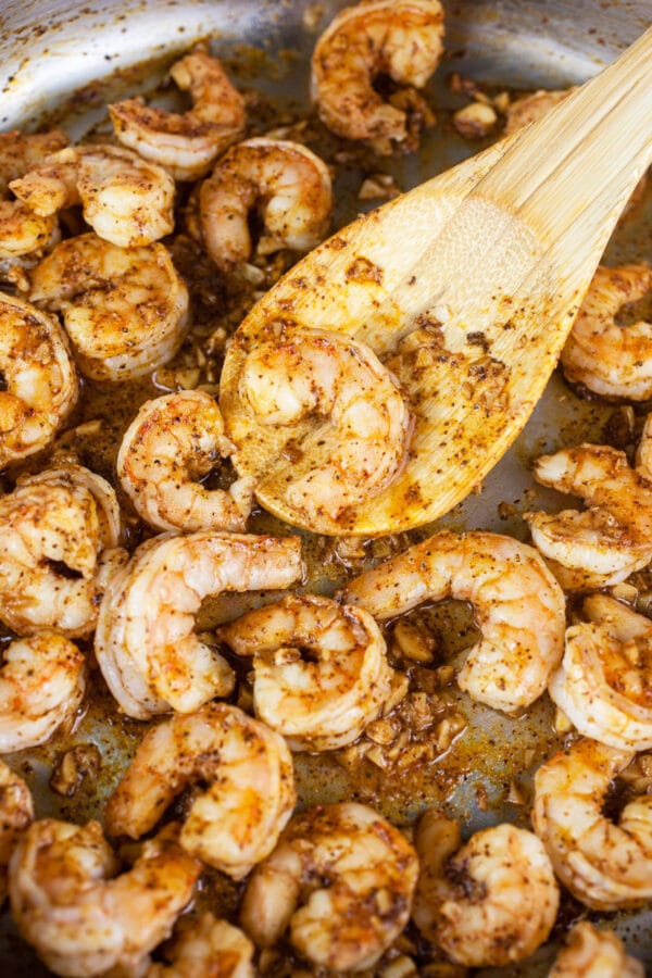 These Mexican Shrimp Rice Bowls are the perfect quick and easy healthy dinner recipe! Rice forms the base of this meal and it's topped with spicy Mexican shrimp, black beans, avocado, and a simple creamy cilantro lime dressing. This delicious dressing is made with sour cream. I love a hearty and flavorful rice bowl! #shrimp #ricebowl #Mexican #cilantro #lime Shrimp sautéed with garlic and spices in skillet.