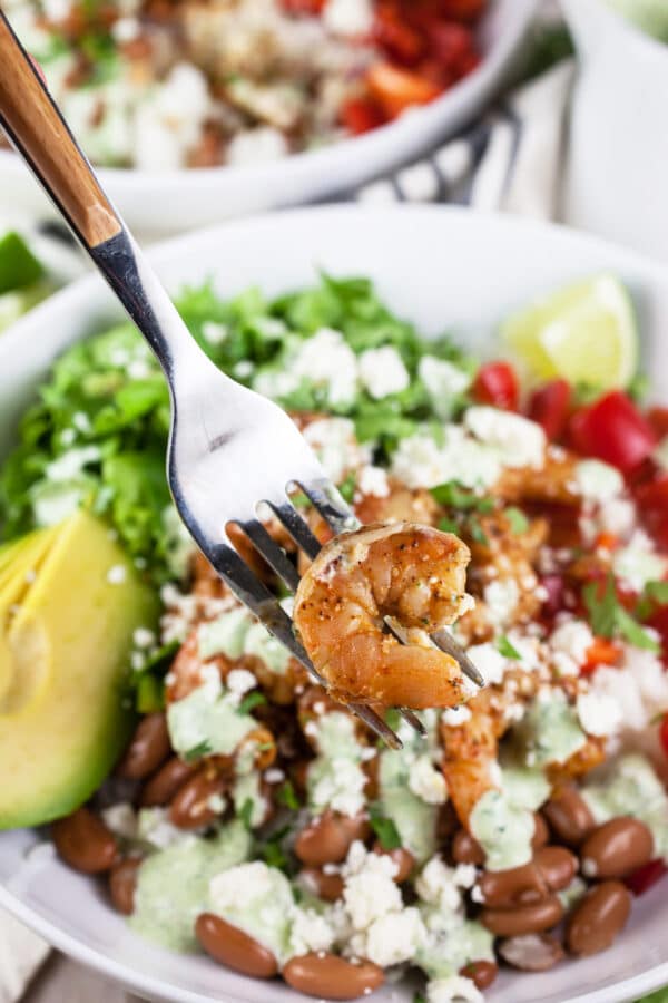 These Mexican Shrimp Rice Bowls are the perfect quick and easy healthy dinner recipe! Rice forms the base of this meal and it's topped with spicy Mexican shrimp, black beans, avocado, and a simple creamy cilantro lime dressing. This delicious dressing is made with sour cream. I love a hearty and flavorful rice bowl! #shrimp #ricebowl #Mexican #cilantro #lime Cooked shrimp on fork lifted from Mexican rice bowl.