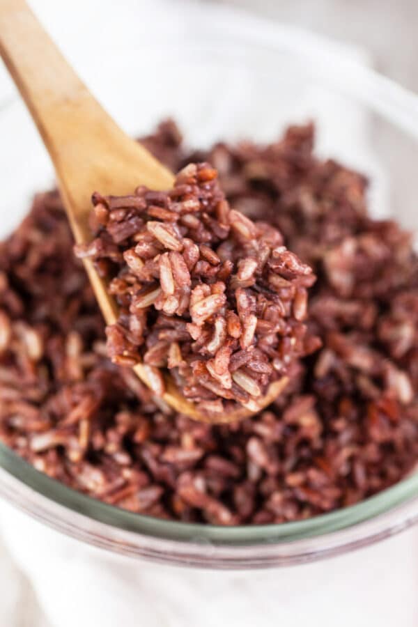 Cooked wild rice on wooden spoon lifted from small glass bowl.