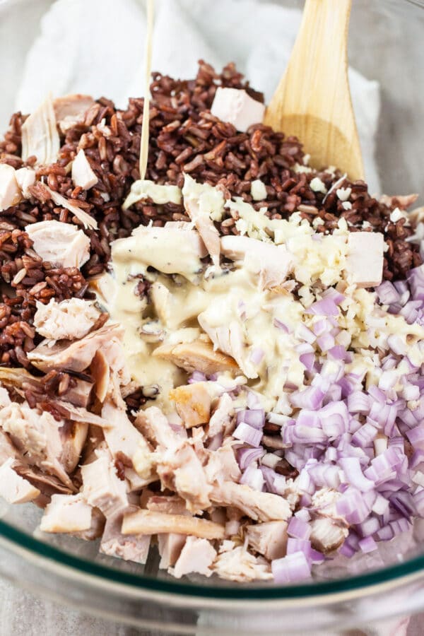 Dressing poured onto cooked wild rice, rotisserie chicken, and shallots in glass bowl.