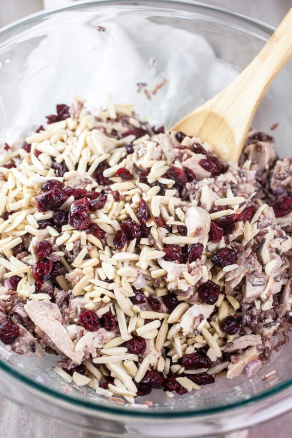 Dried cranberries and sliced almonds on top of chicken salad in glass bowl.