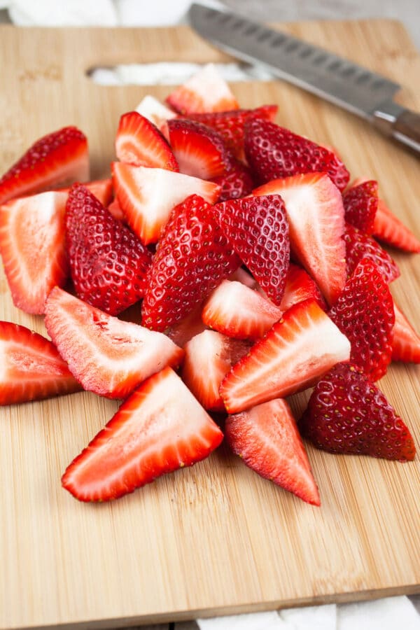 Sliced fresh strawberries on wooden cutting board with knife.