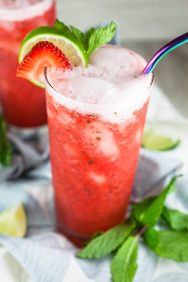 Virgin strawberry mojitos with fresh mint and limes in tall glass with metal straw.
