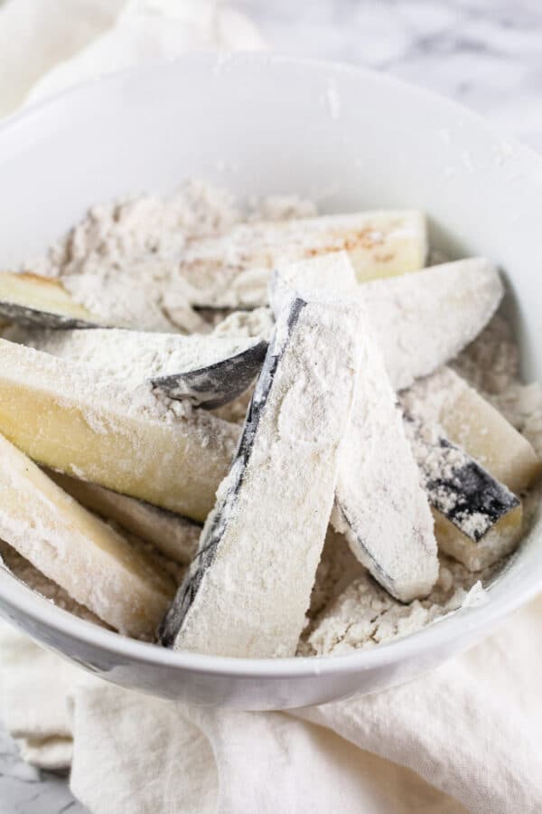 Eggplant fries coated in flour in white bowl.