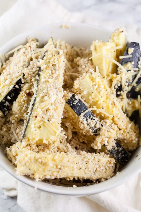 Eggplant fries coated in Parmesan breadcrumb mixture in white bowl.
