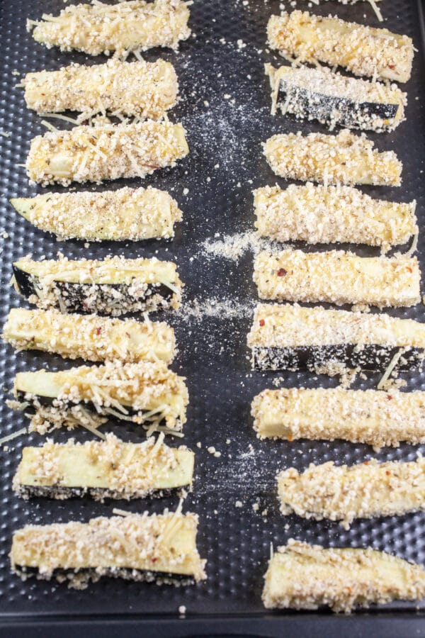 Uncooked coated eggplant fries on baking sheet.