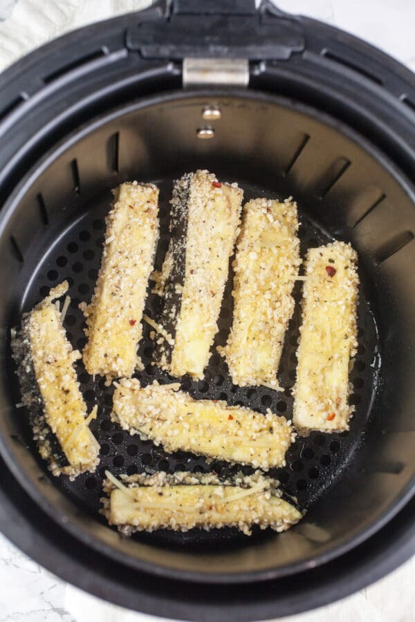 Uncooked eggplant fries in air fryer basket.