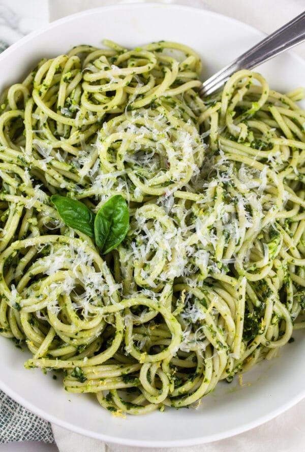 Spaghetti noodles tossed in green pasta sauce in white bowl topped with Parmesan cheese.