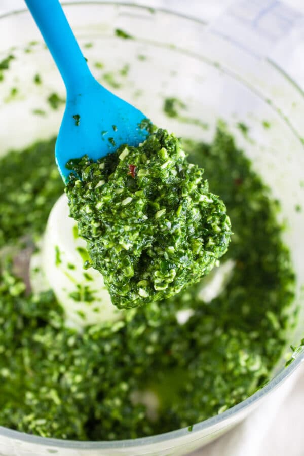 Blue spatula lifting spinach basil pasta sauce from food processor.