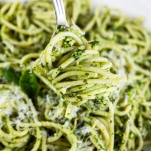 Pasta tossed in green pasta sauce on fork.